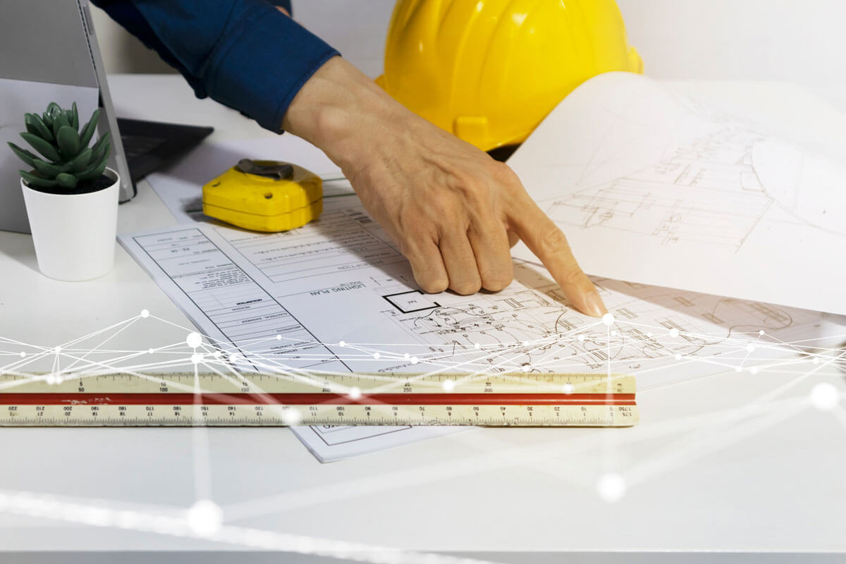 Hand pointing at construction blueprint on desk.